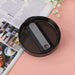 Black circular object with a gray center on a pink surface with a magazine underneath