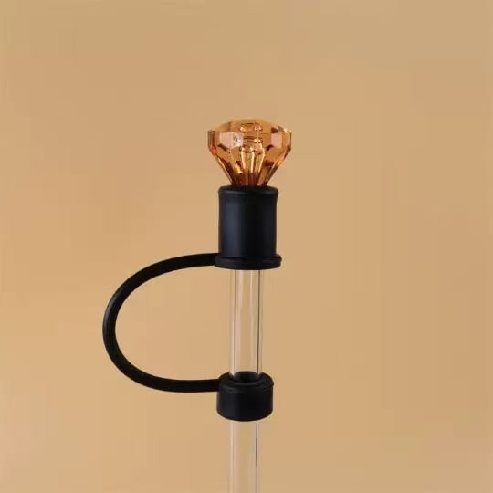 Decorative lamp with a clear glass base, black accents, and an amber-colored bulb on a beige background.