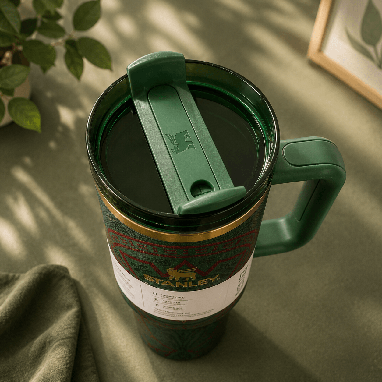 Green Stanley mug with a lid on a green surface with a plant in the background