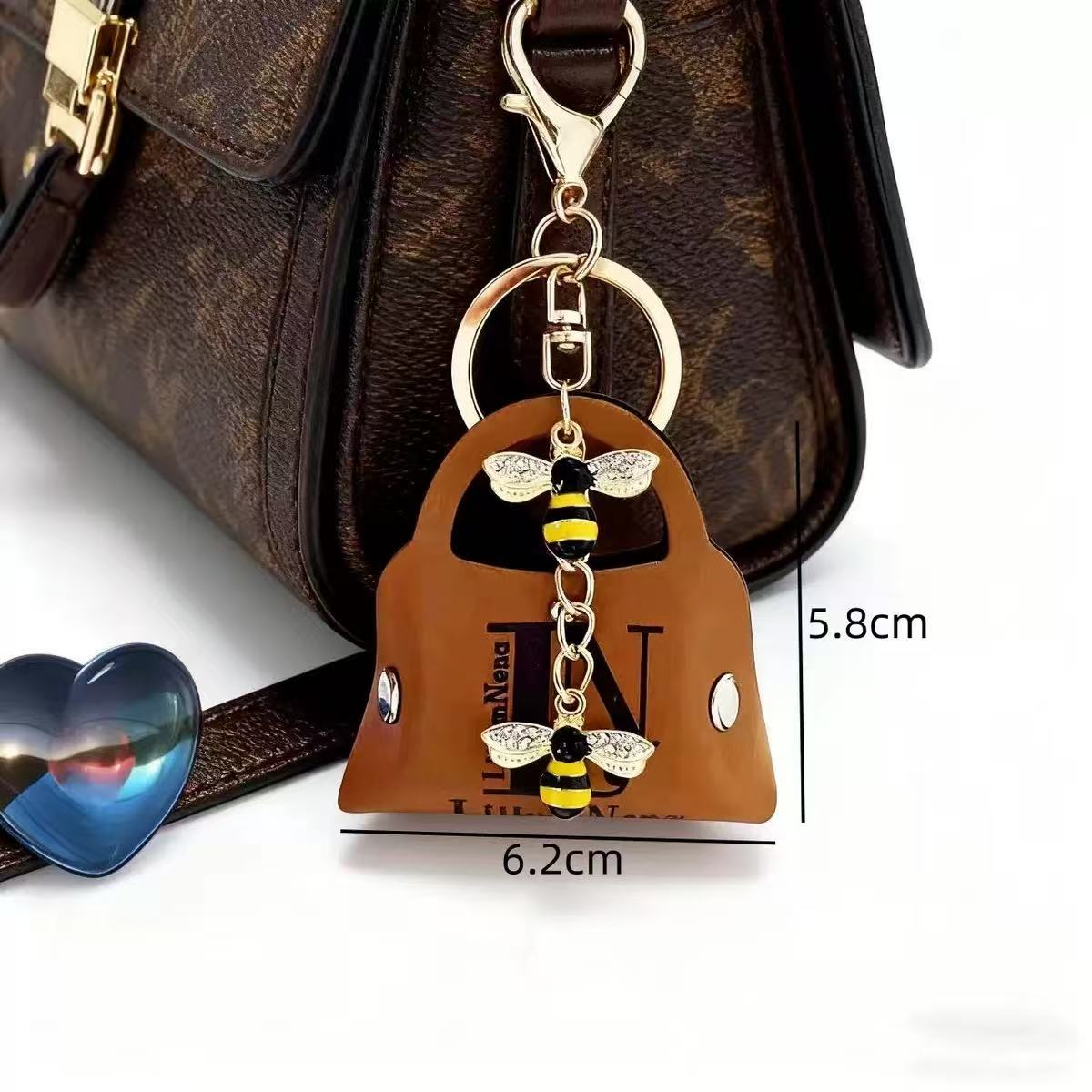 Keychain with bee design attached to a brown handbag, with measurements displayed.