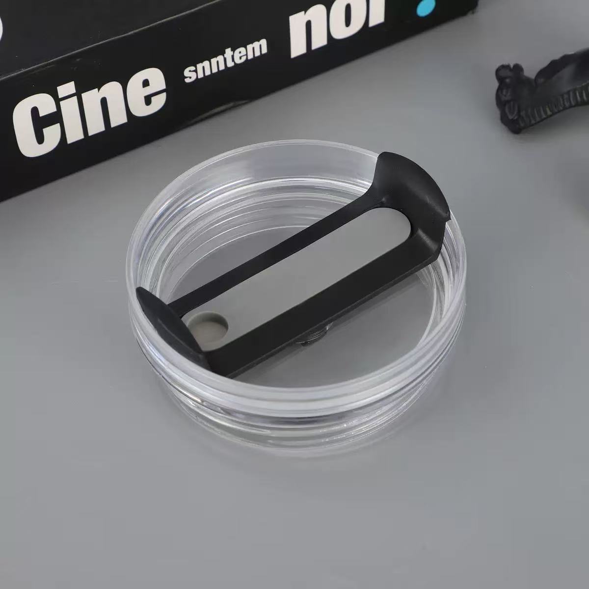Clear container with black lid on a gray surface, with 'Cine' branding in the background.