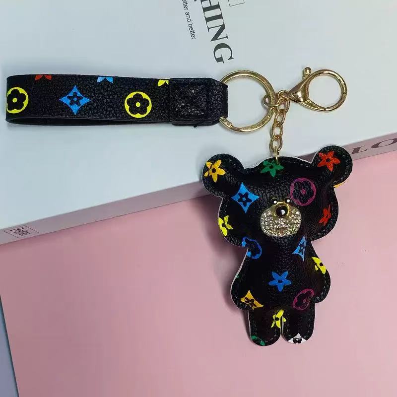 Black bear-shaped keychain with colorful patterns on a pink surface