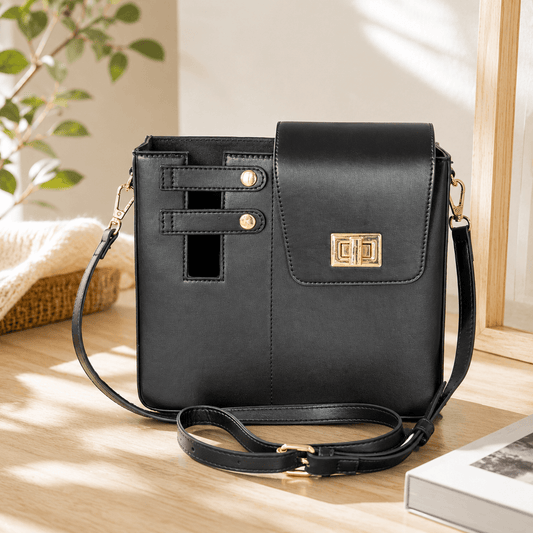 Black handbag with gold accents on a wooden surface with a plant in the background