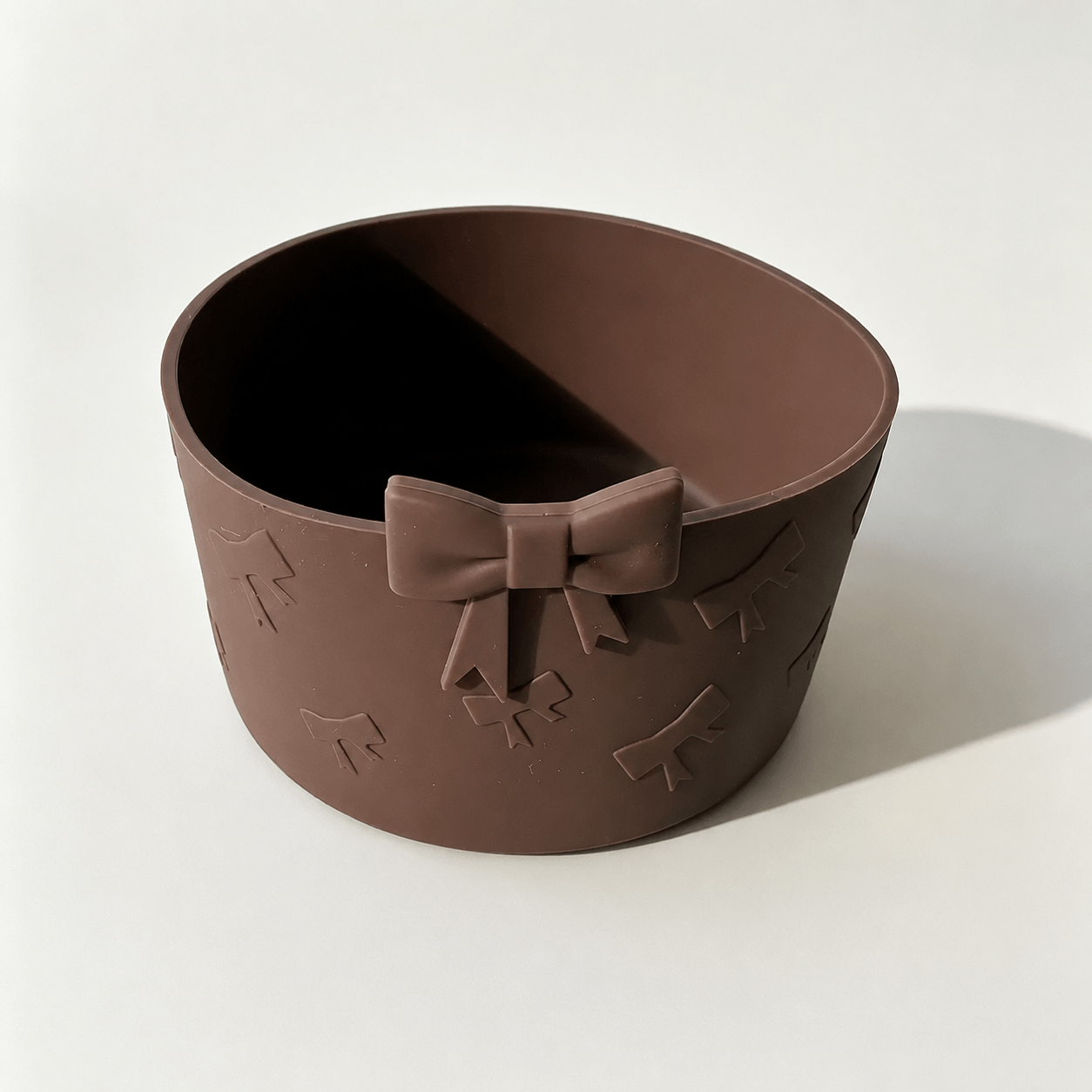 Brown silicone tumbler boot sleeve with an embossed bow pattern and decorative bow accent, designed to fit tumblers with a 7.5 cm base diameter for added protection and style.