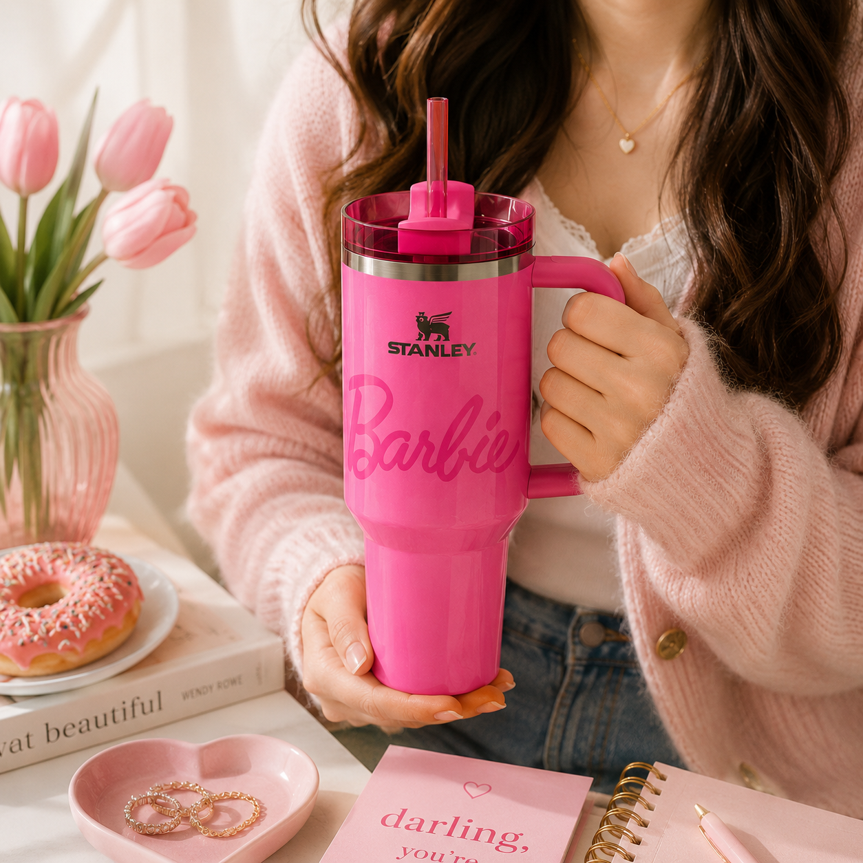 Person holding a pink Stanley Barbie mug with tulips and a donut in the background