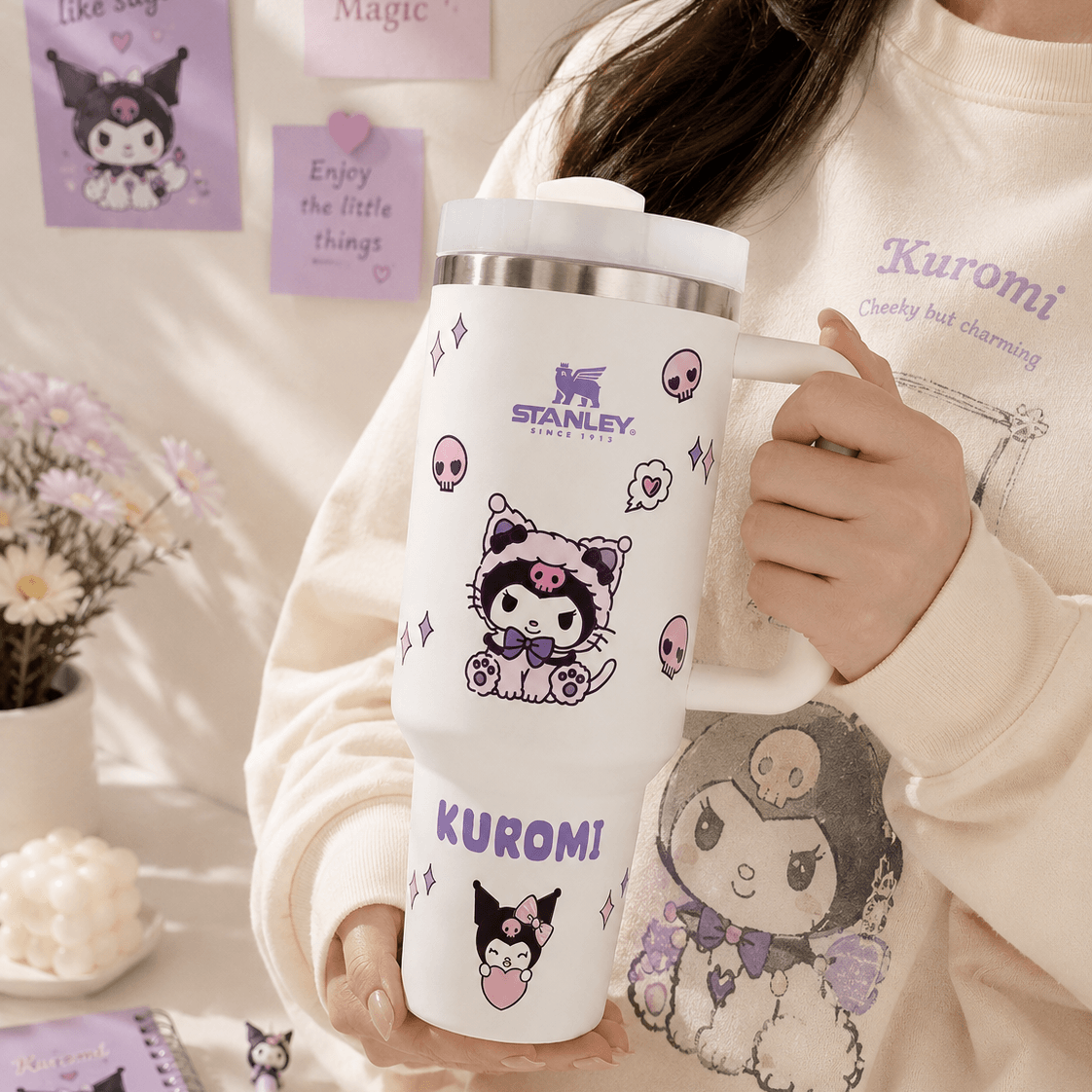 Person holding a Stanley tumbler with Kuromi character designs, surrounded by decorative elements.