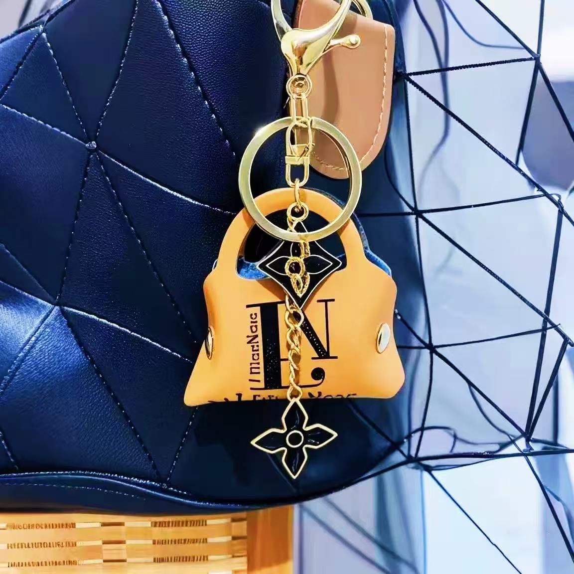 Gold keychain shaped like a handbag with a chain detail on a blue textured surface.