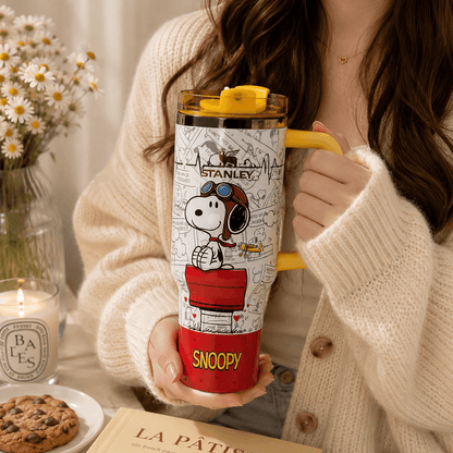 Person holding a Snoopy-themed Stanley tumbler with a cozy indoor setting.