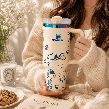Person holding a Snoopy-themed Stanley mug with a cozy indoor setting.