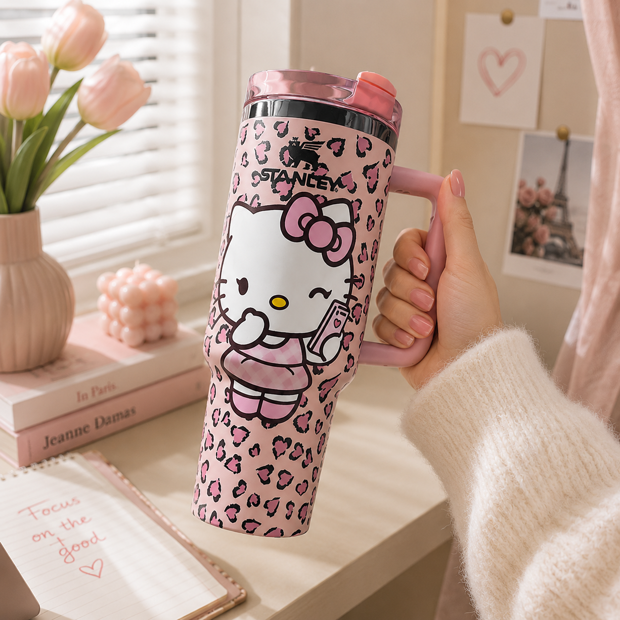 Person holding a pink Hello Kitty mug with a leopard print pattern on a desk.
