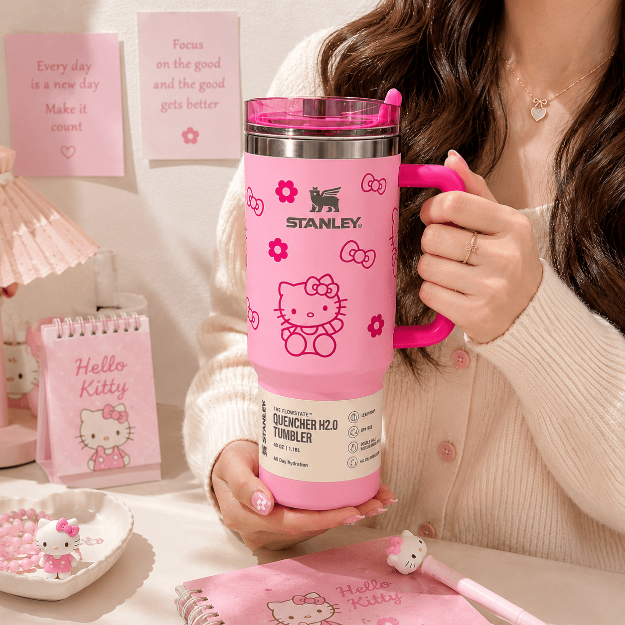 Person holding a pink Stanley Hello Kitty water bottle with stationery items in the background.