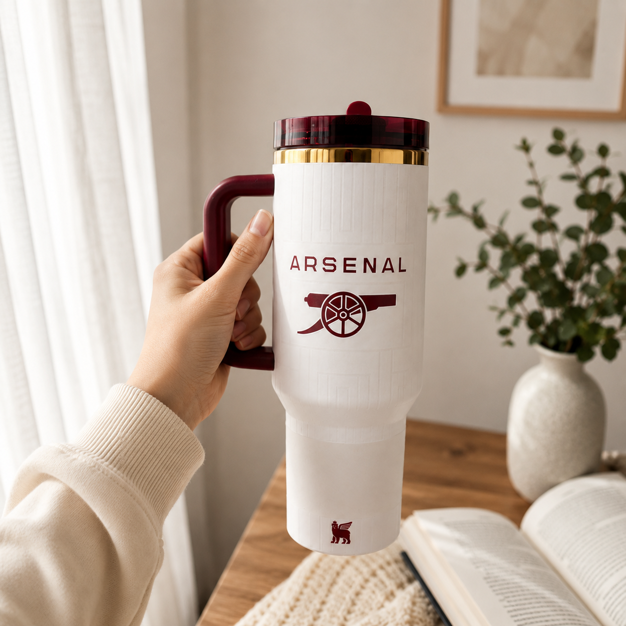 Person holding a white mug with Arsenal logo in a cozy indoor setting