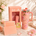 Pink Stanley mug with floral design, gift box, and card on a soft surface with flowers.