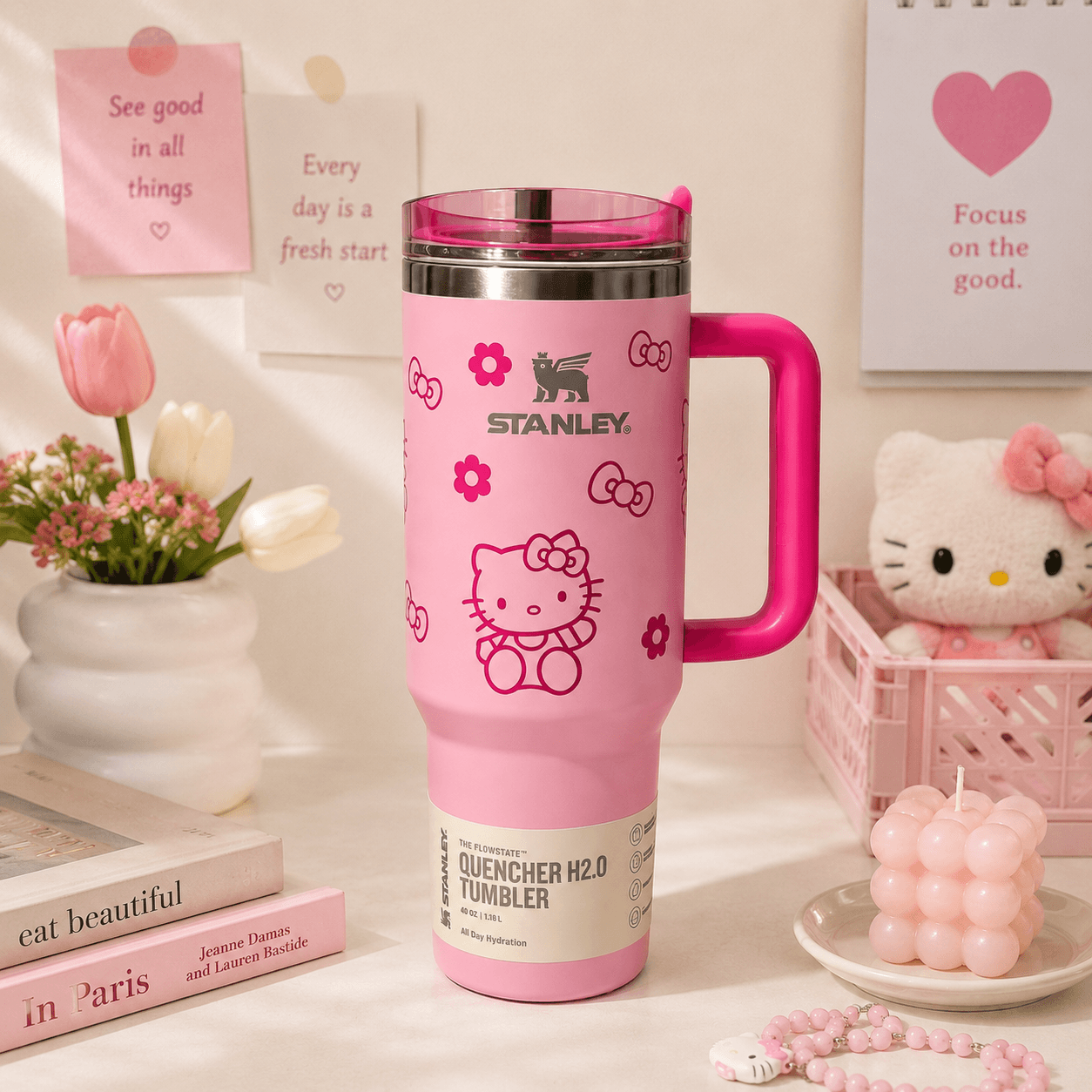 Pink Stanley tumbler with Hello Kitty designs on a decorative surface with flowers and books.
