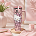 Pink travel mug with Hello Kitty design on a desk with flowers and stationery.