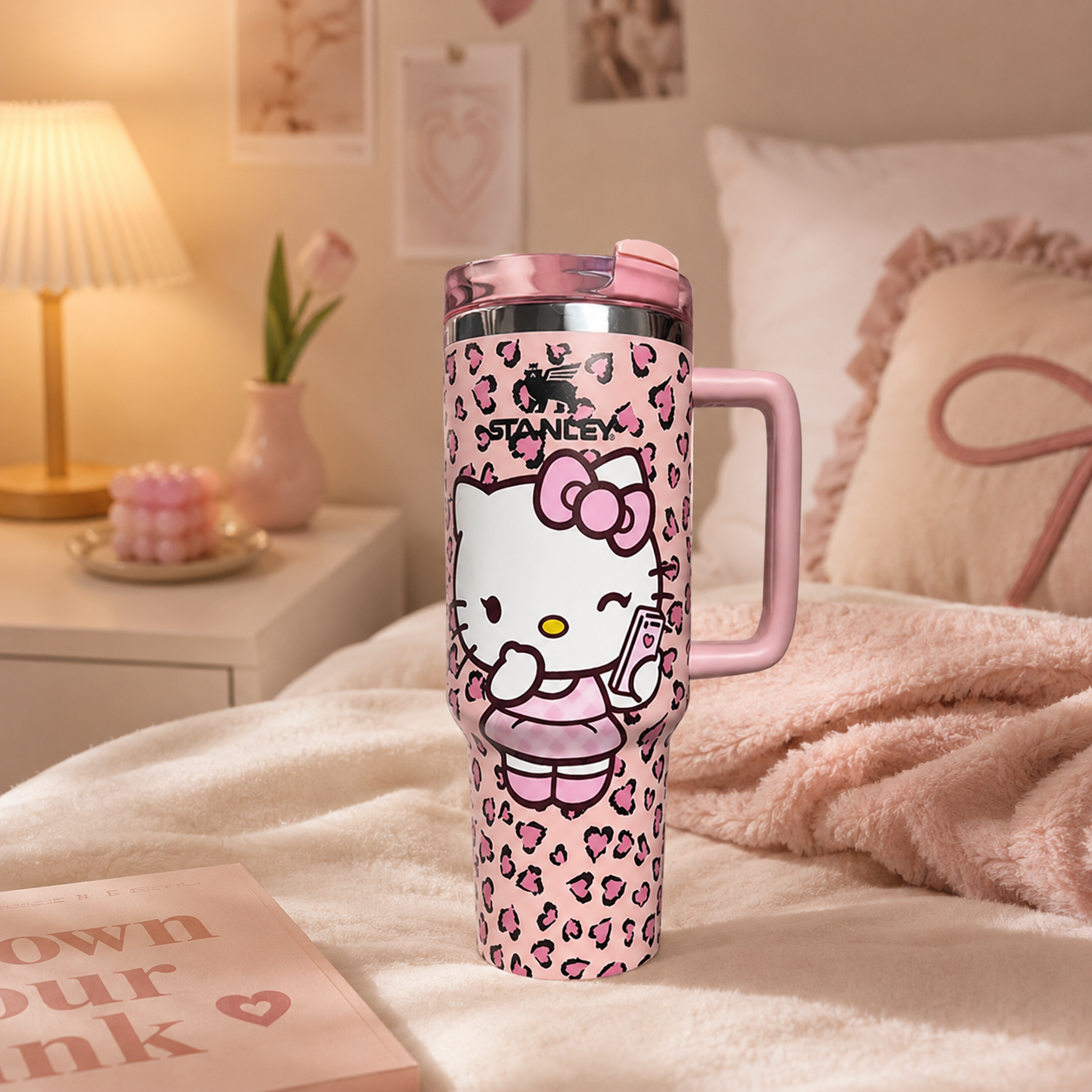 Pink tumbler with Hello Kitty design on a bed in a cozy room.
