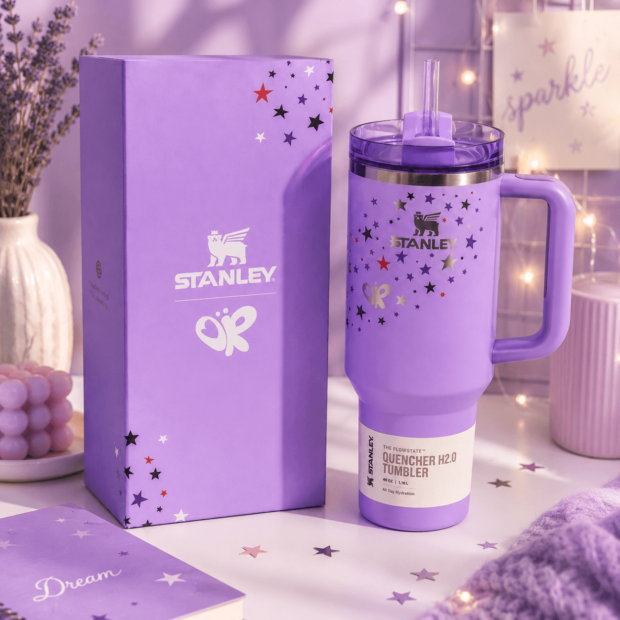 Purple Stanley tumbler with stars and handle on a matching box against a soft purple background.