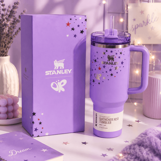 Purple Stanley tumbler with stars and handle on a matching box against a soft purple background.