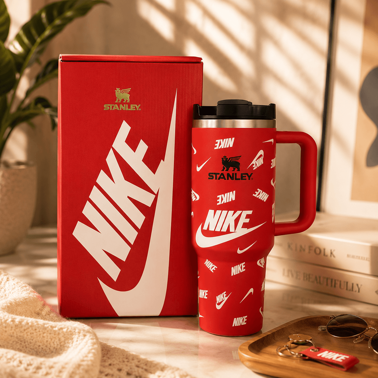Red Stanley mug with Nike logo on a surface with books and plant in the background