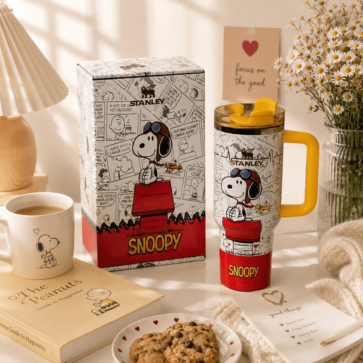 Snoopy-themed Stanley mug on a table with a book and cookies.