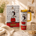 Stanley Snoopy mug with packaging on a table with flowers and cookies.