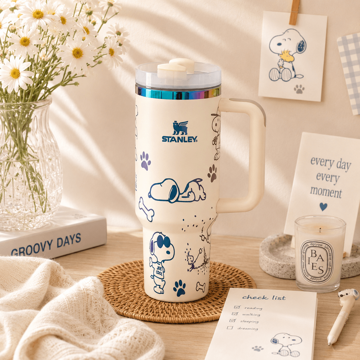 Stanley mug with Snoopy design on a table with flowers and stationery