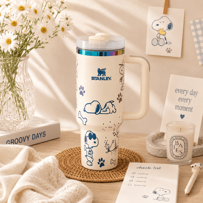 Stanley mug with Snoopy design on a table with flowers and stationery