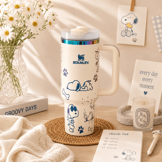 Stanley mug with Snoopy design on a table with flowers and stationery
