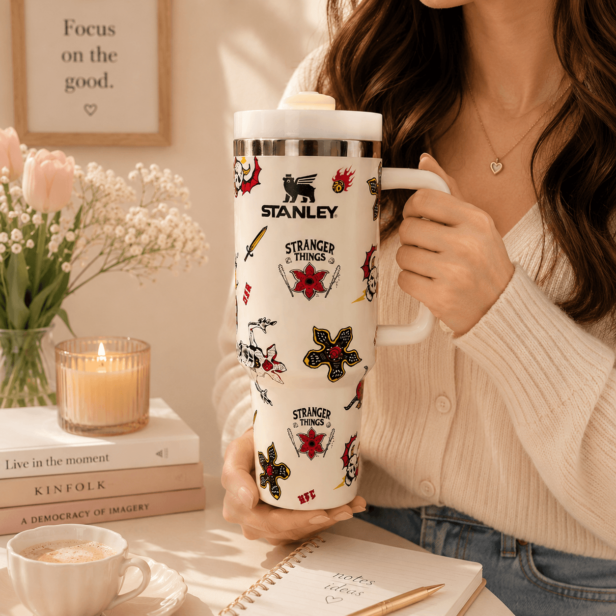 Person holding a Stanley mug with 'Stranger Things' designs in a cozy setting.