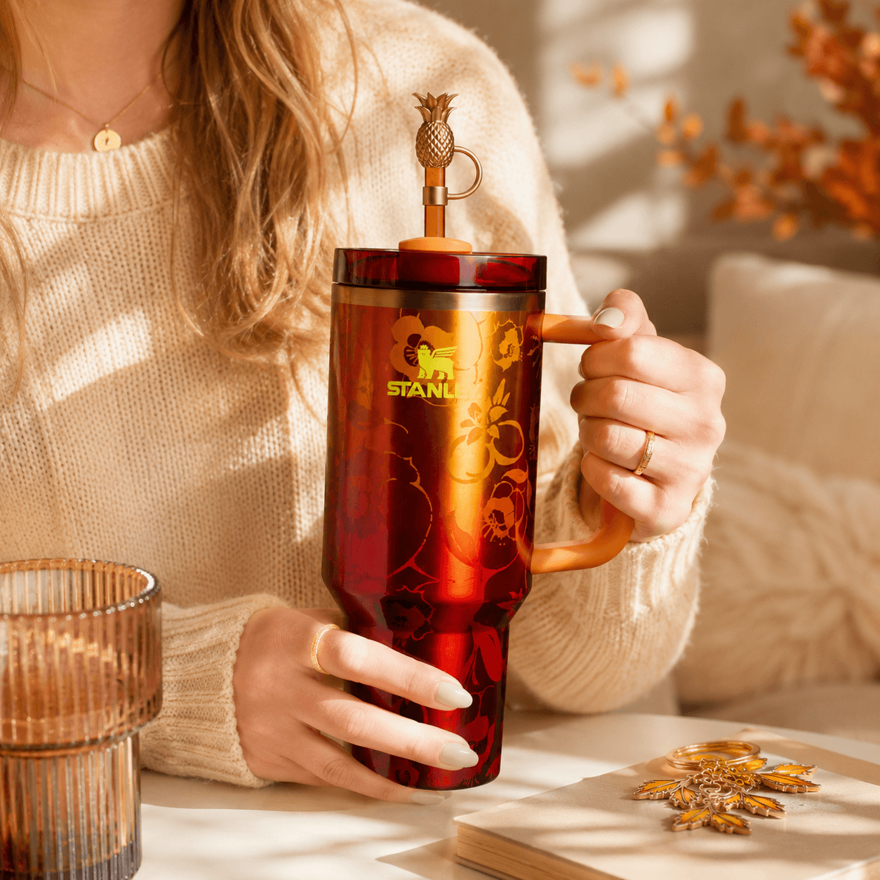 Person holding a red Stanley mug with a decorative lid in a warm, indoor setting.