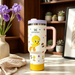 Stanley mug with cartoon character on a table with flowers and plants in the background