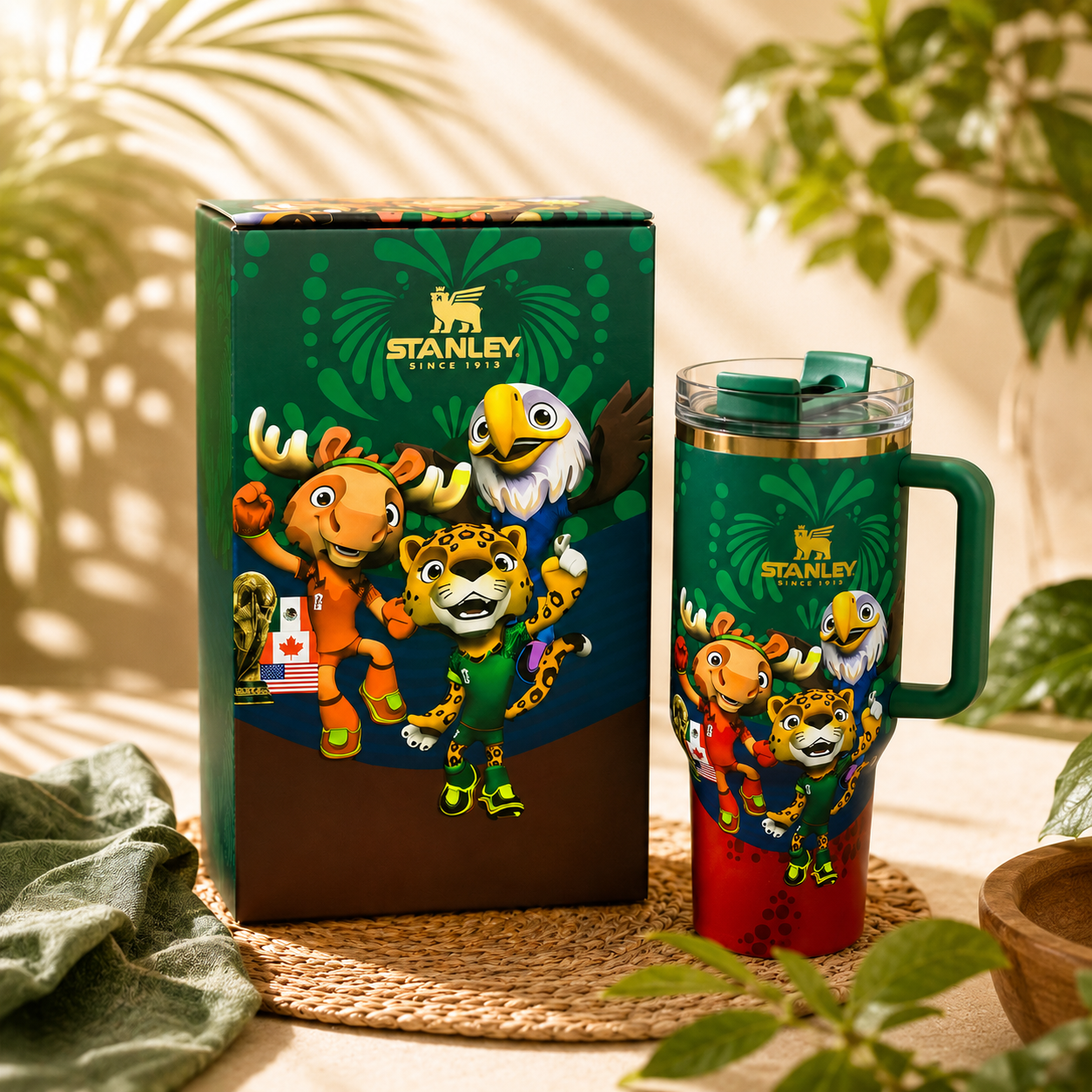 Stanley mug with colorful animal designs next to its packaging on a table with plants in the background