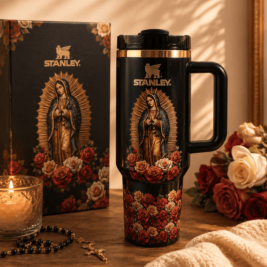 Stanley mug with religious design featuring a figure and roses on a wooden surface with flowers and a candle.