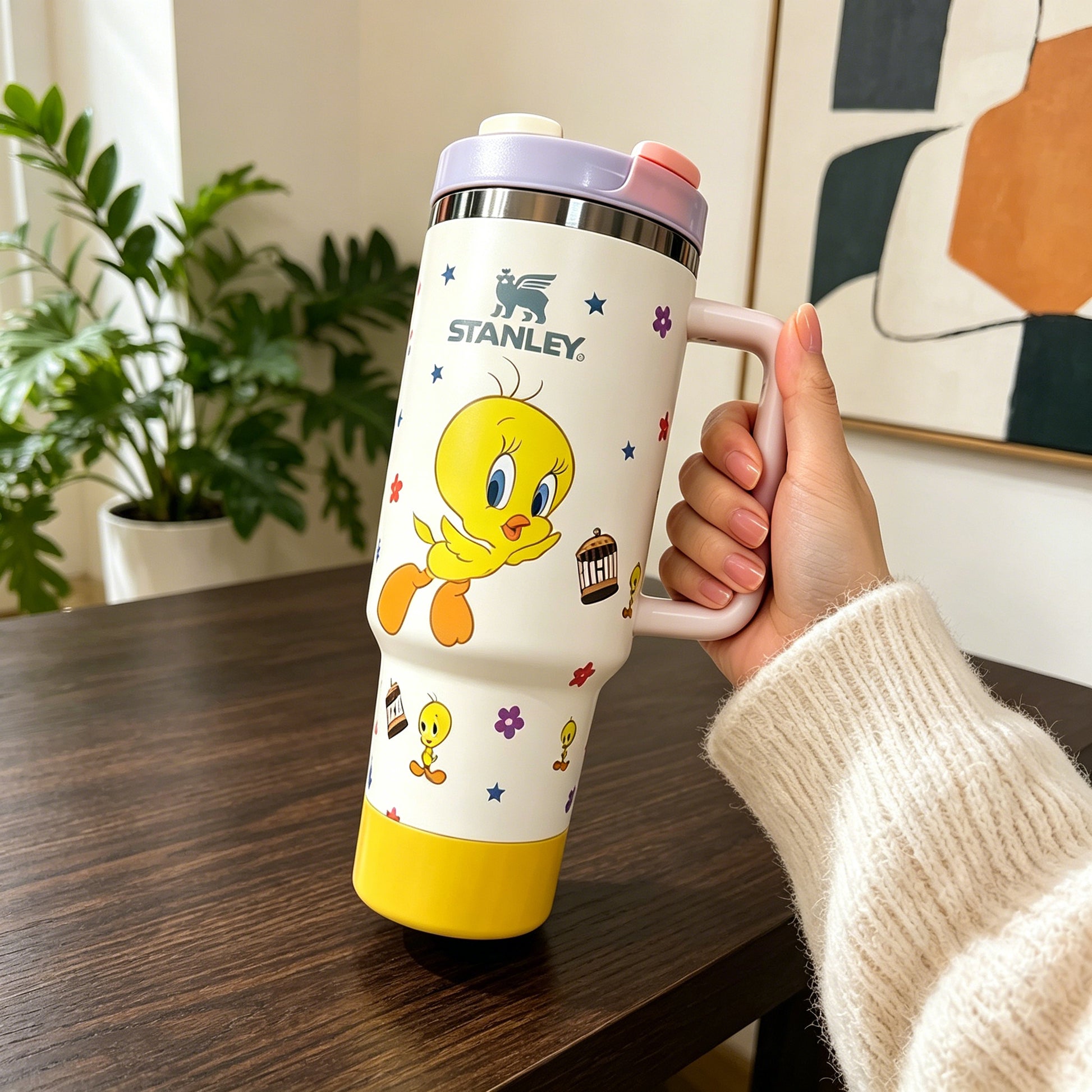Person holding a Stanley tumbler with Looney Tunes design on a wooden table.