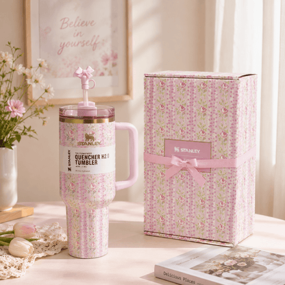 Stanley tumbler with floral design next to its packaging on a decorative surface.