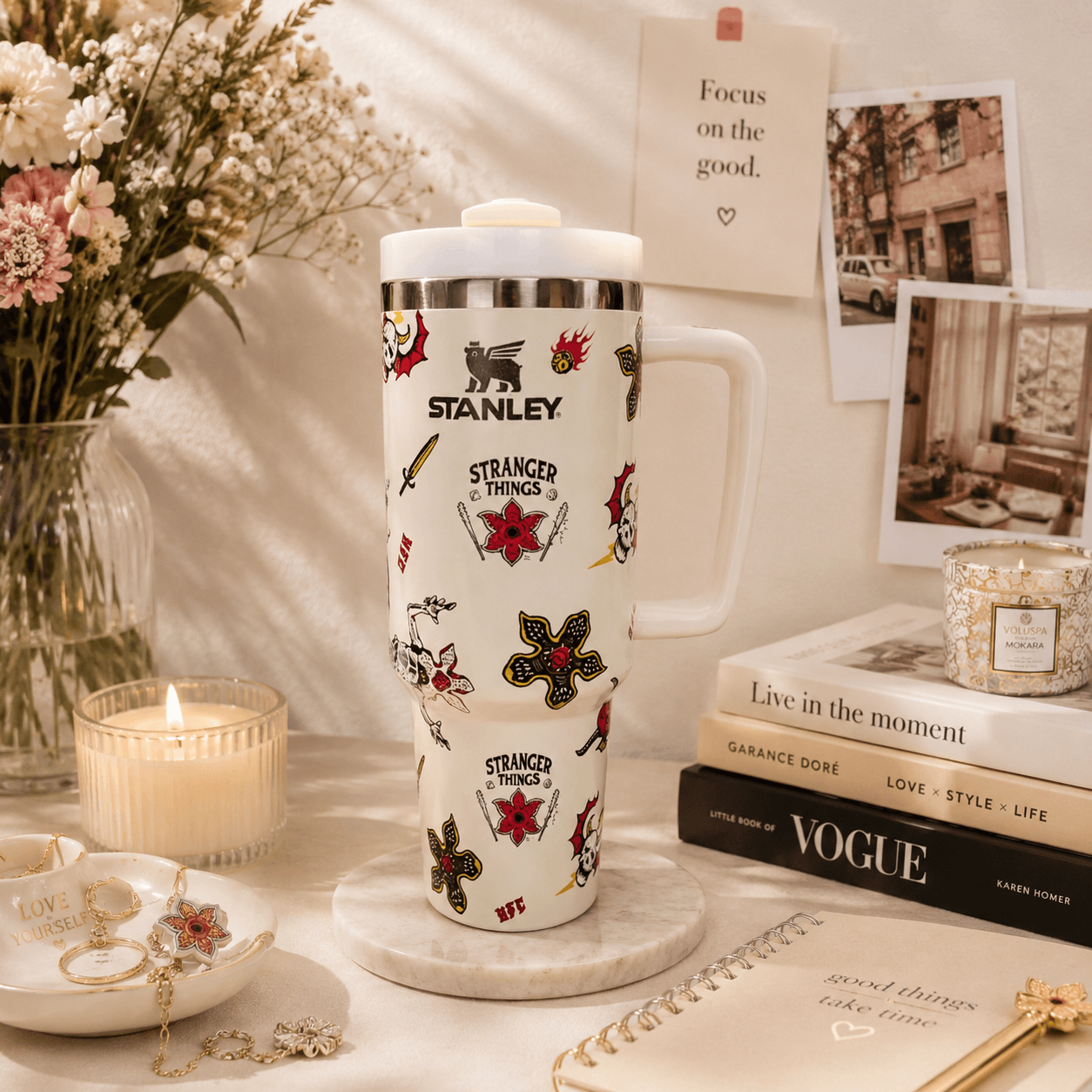 Stanley mug with 'Stranger Things' designs on a decorative table with books and flowers.