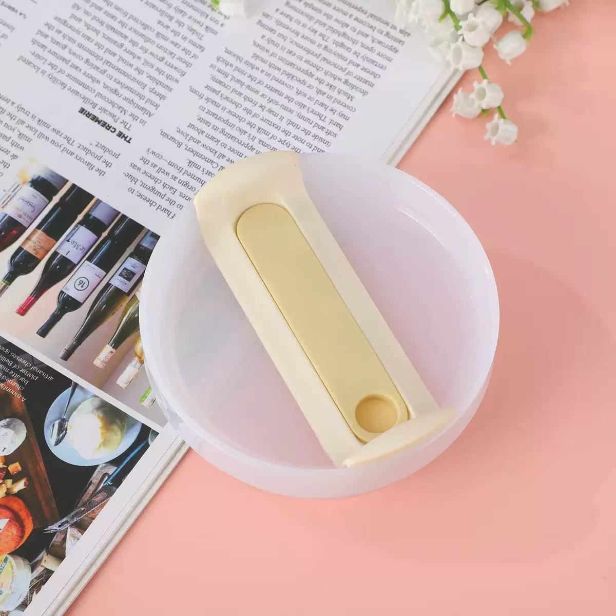 White bowl with beige handle on a pink surface with a magazine underneath