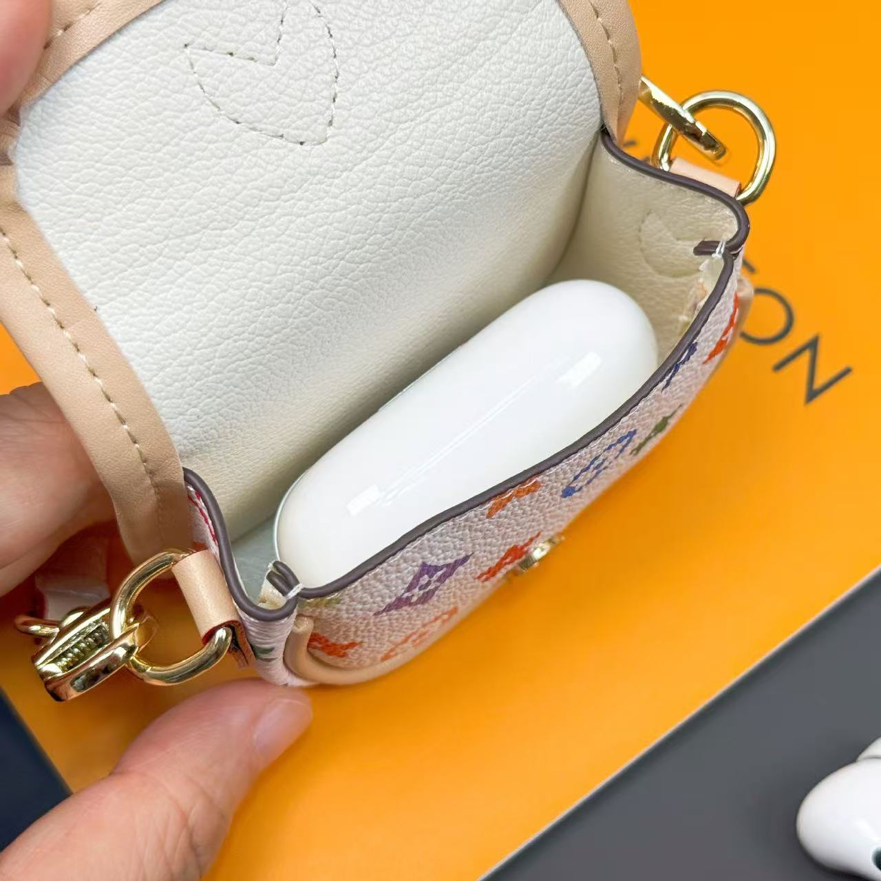 White earbuds in a small pouch held by a hand on an orange background