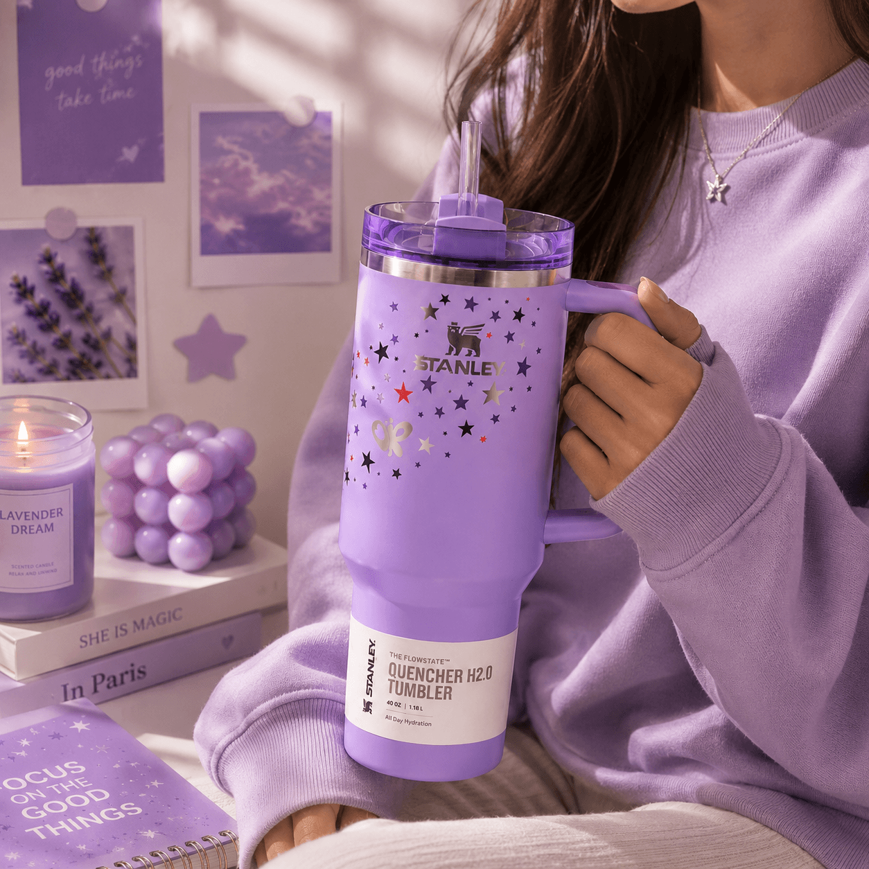 Person holding a purple Stanley tumbler with decorative elements in a cozy setting.