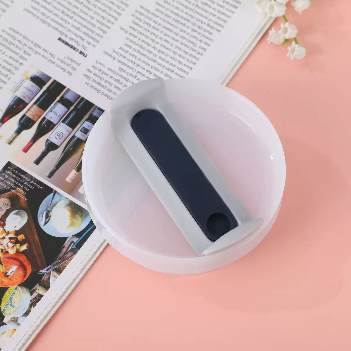 White dish with a blue handle on a pink surface with a magazine underneath