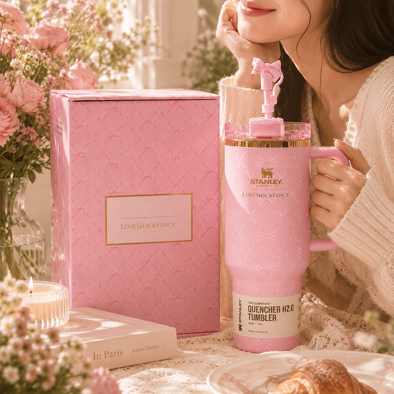 Pink Stanley tumbler with a woman holding it, surrounded by flowers and a pink box.